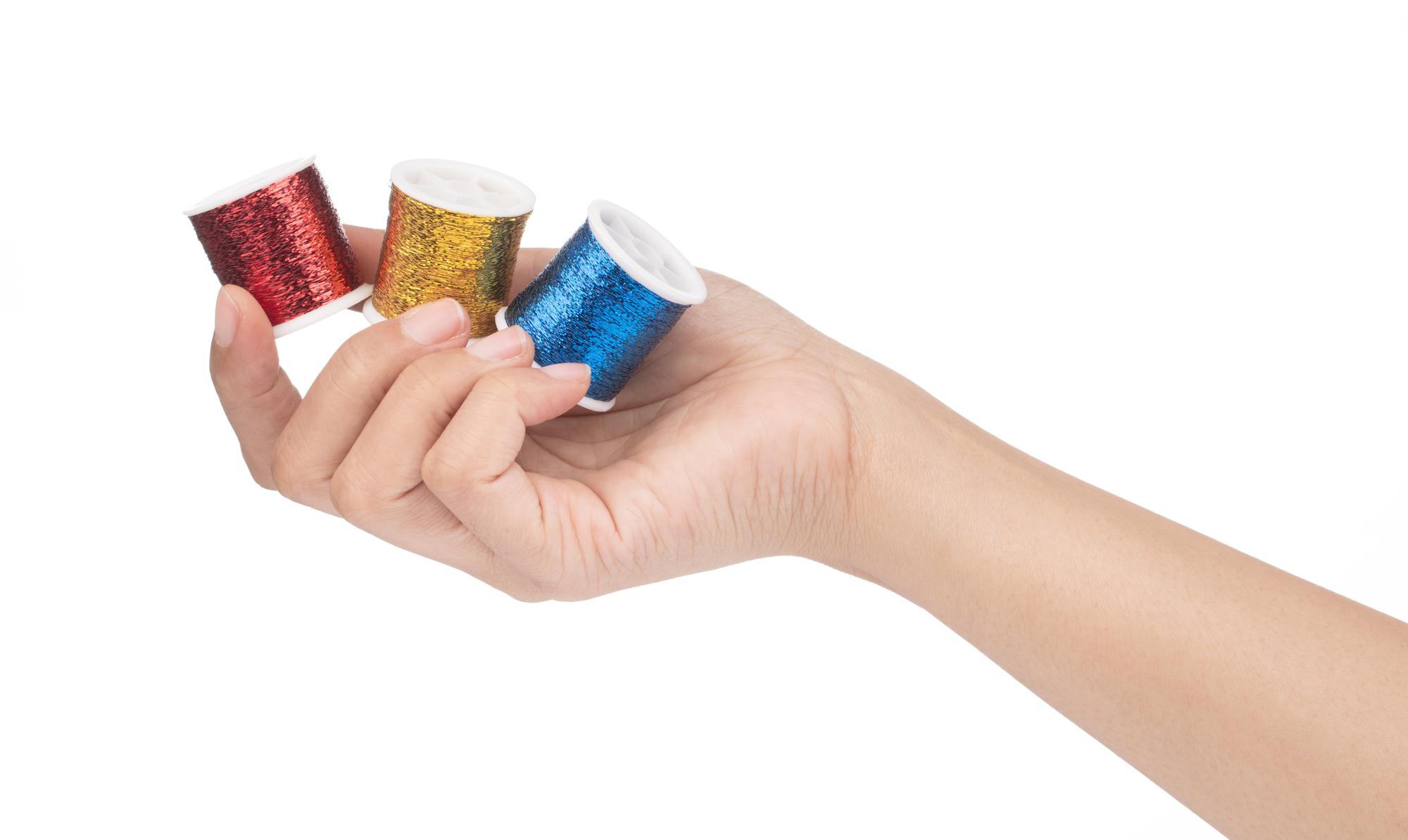Mano che guida un filo colorato su un tessuto bianco